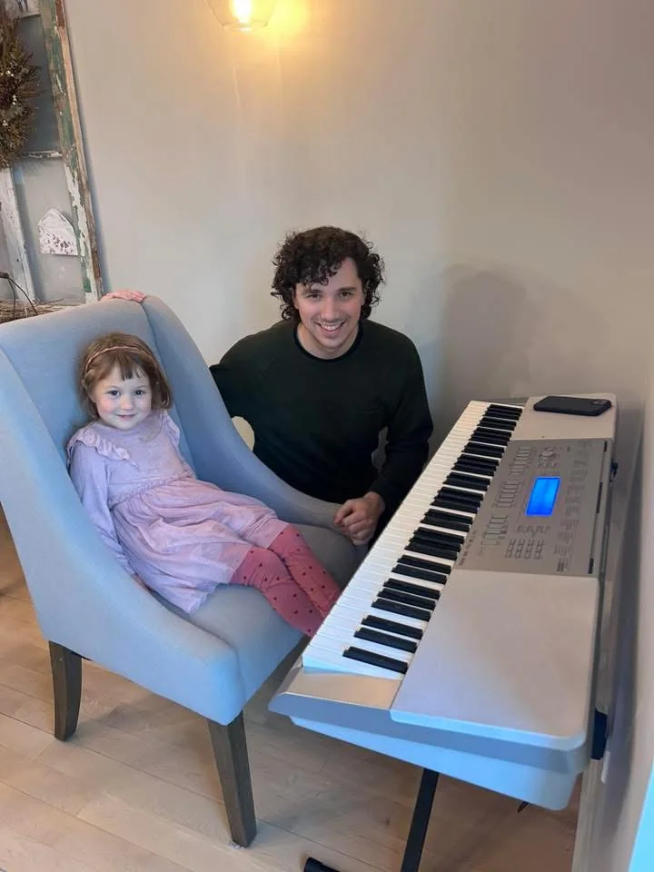 A young piano student with a teacher beside a keyboard